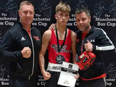 Two coaches either side of a young boxer holding a Manchester Box Cup certificate at Warriors Boxing Academy
